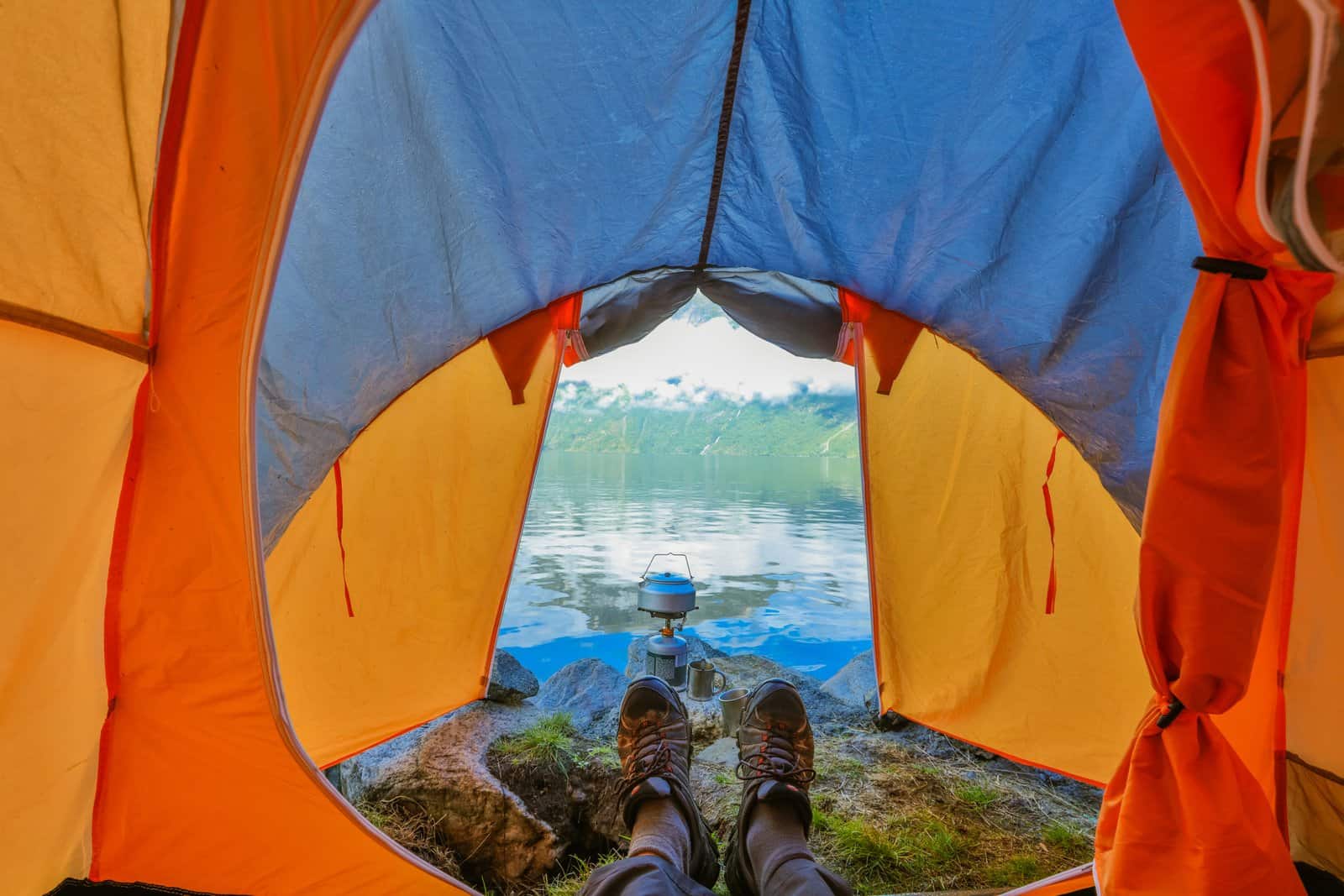 Guy in trekking boots is in a tent. View of the fjord in Norway. 