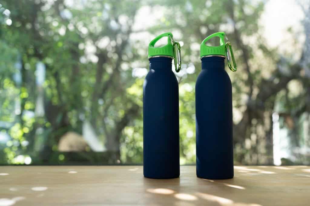 Two blue minimal reusable water bottle is sitting on a wood table with natural sunlight