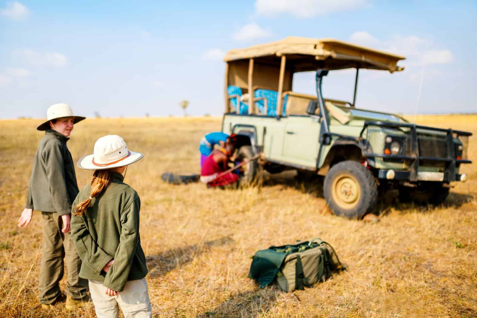 Kids in Kenya safari on morning game drive in open vehicle looking at maasai guides 