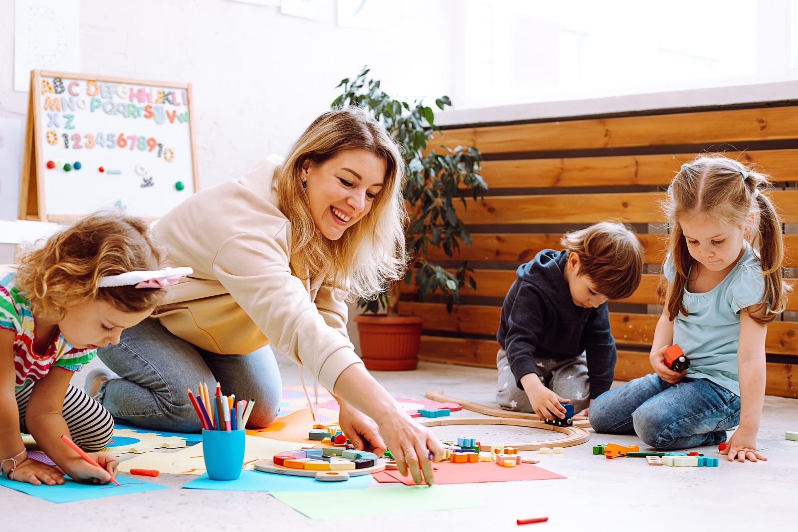 An educator sitting on the floor playing with children in a kindergarten classroom