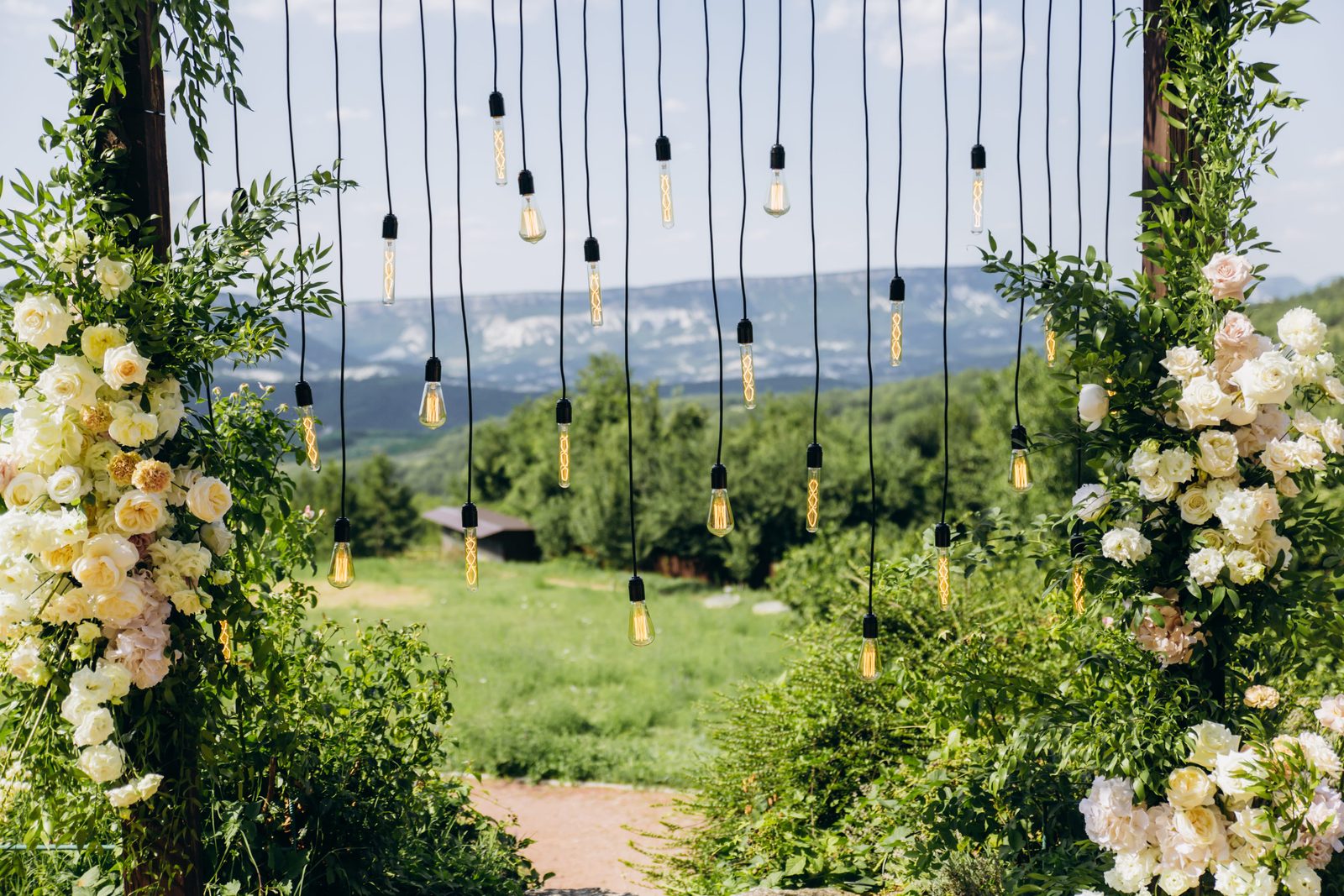 A rustic wedding arch with white flowers and string lights in a park