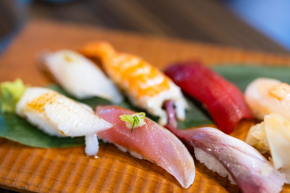 A row of nigiri sushi on a bamboo leaf, including salmon, tuna, squid and yellowtail