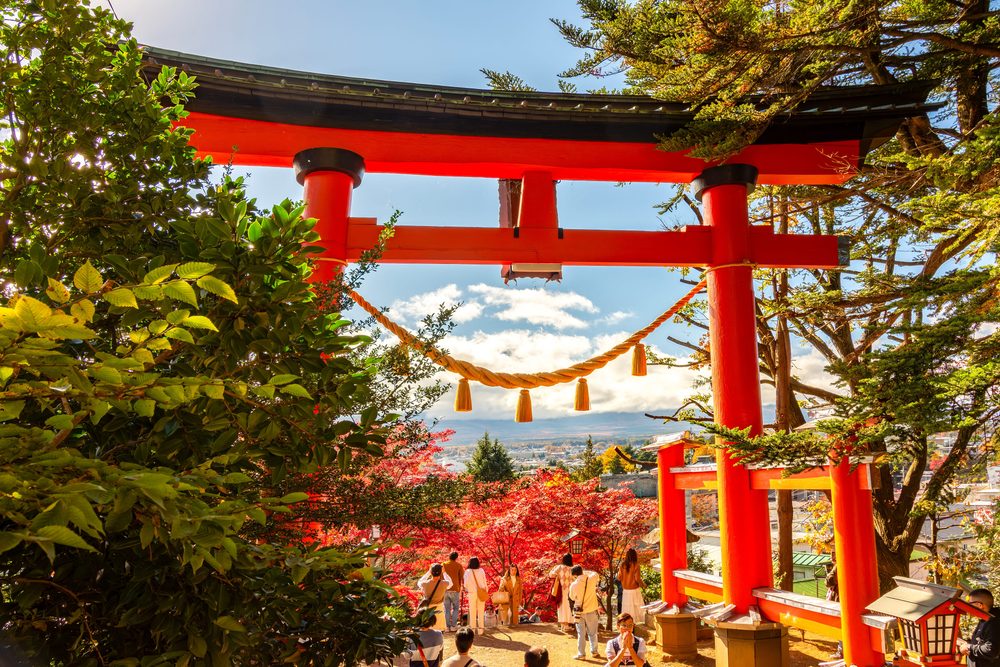 A red torii gate at Arakura looking down over autumn maples toward the Fuji five lakes valley