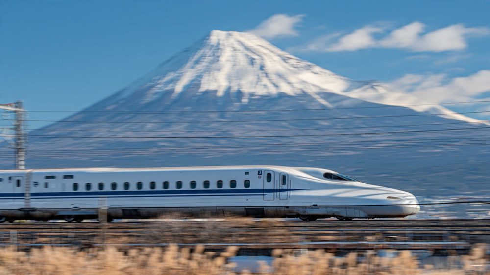 A shinkansen bullet train running past the snow-capped cone of Mount Fuji