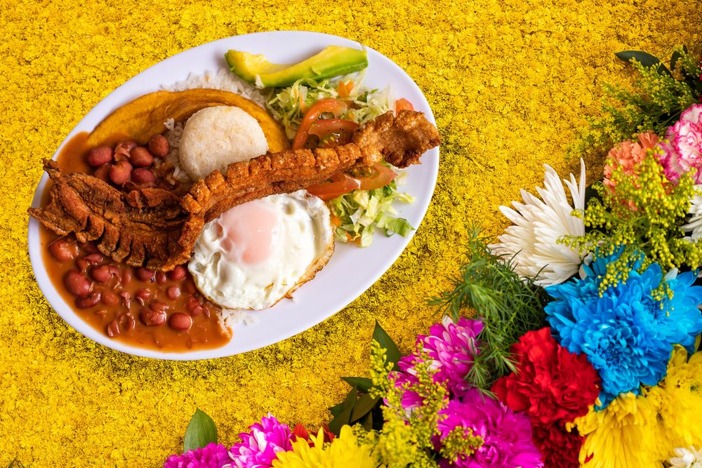 A bandeja paisa of beans, rice, chicharron, fried egg, plantain and arepa, on a bed of flowers
