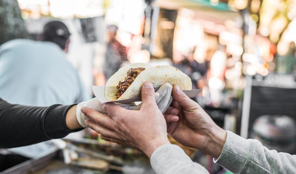A filled taco passed across the counter at a Mexican street food stall