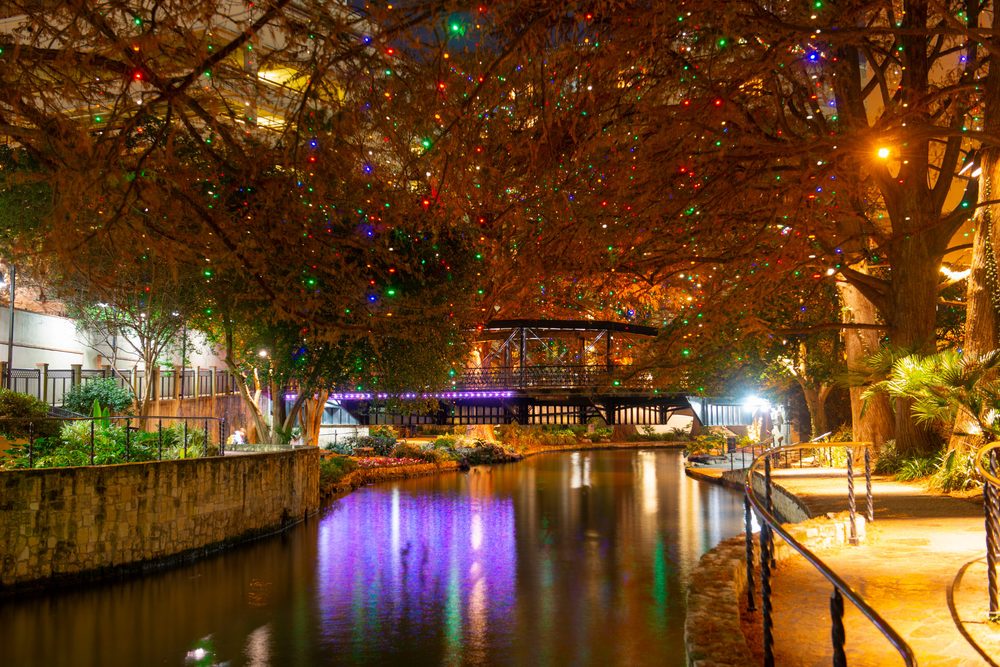 The San Antonio River Walk at night, cypress trees strung with coloured lights above the water