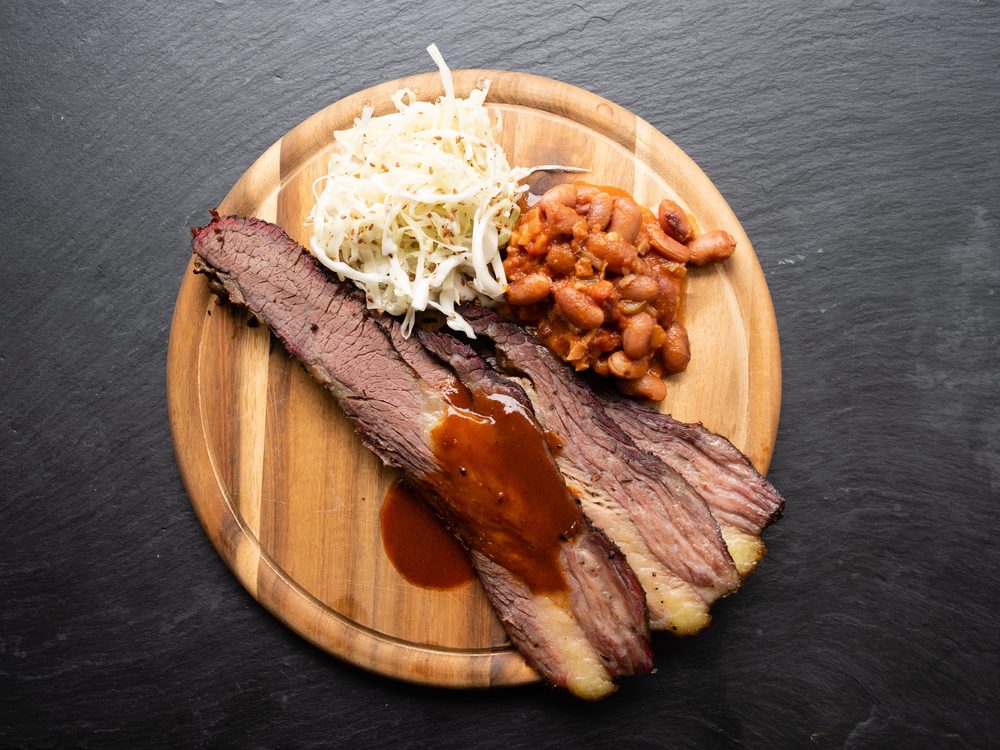 Sliced Texas brisket on a wooden board with pinto beans, coleslaw and red sauce