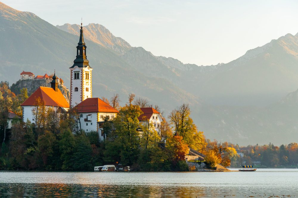 The pilgrimage church on Lake Bled's island in autumn light, with Bled Castle on the cliff behind